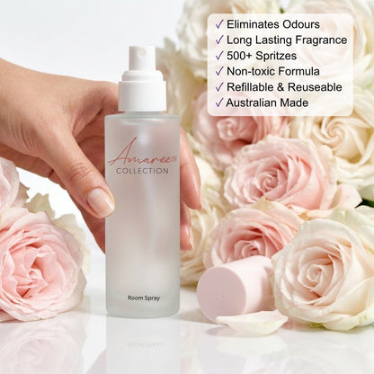 A frosted glass room spray bottle with a white pump is held by a hand, surrounded by pink and white roses. A white text box on the right lists product benefits in bullet points.