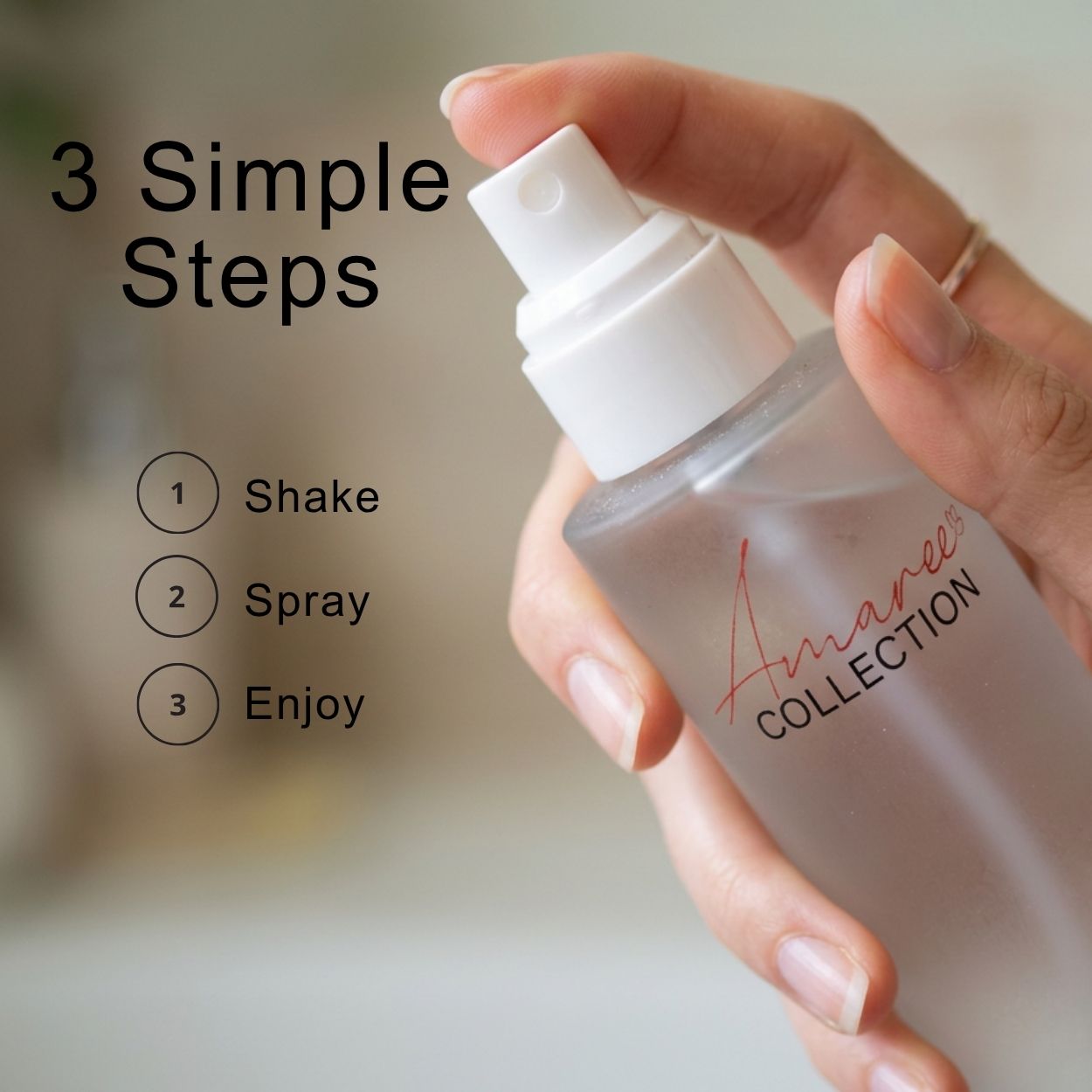 A hand holding a frosted glass spray bottle with a white pump dispenser. The bottle has a red script logo reading &