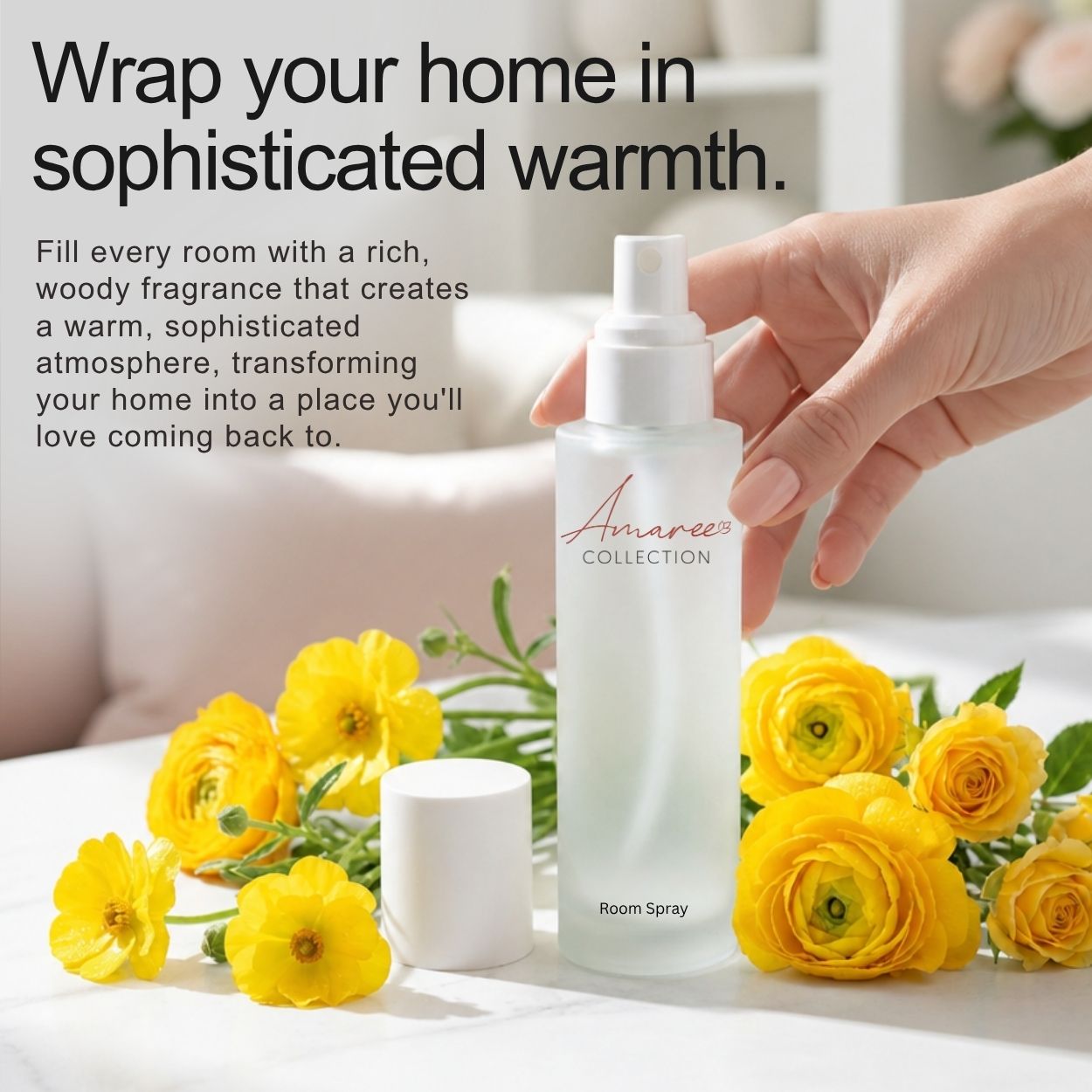 A hand holds a frosted white bottle of Amaree Collection Room Spray next to its white cap, styled with bright yellow flowers on a white surface. Text on the left reads, &