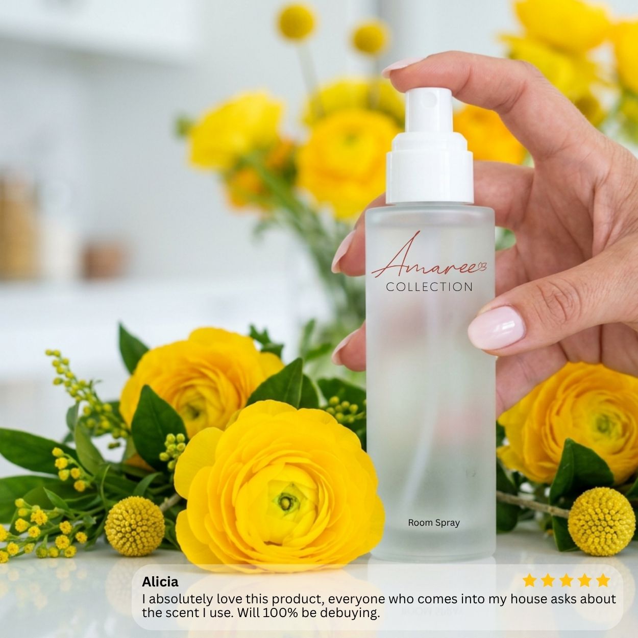 A hand holds a frosted glass room spray bottle with a white pump dispenser. The bottle is labeled &